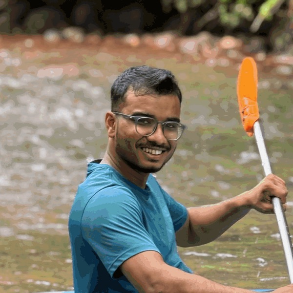 Deepak R smiling from a blue kayak on a river