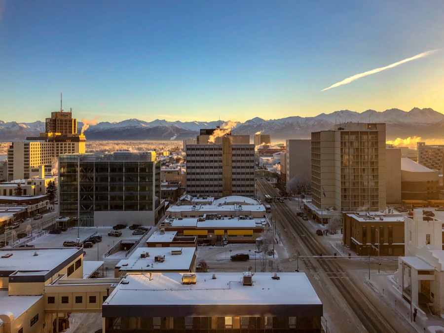 Snow-covered rooftops of downtown Anchorage at sunrise with the Chugach Mountains behind