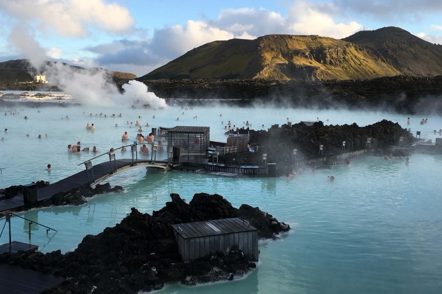 Steam drifting over the milky blue water of the Blue Lagoon, with bathers, boardwalks and lava rock