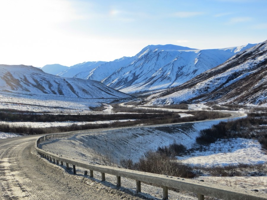 The gravel Dalton Highway curving through a snow-dusted Brooks Range valley in northern Alaska