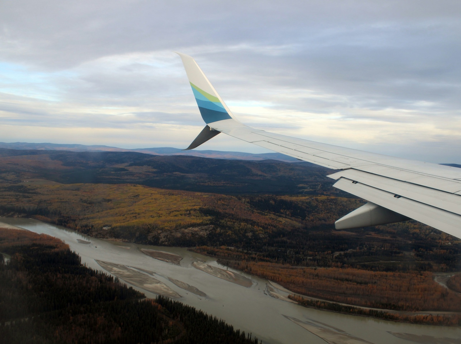 An airliner's wing over autumn forest and a wide braided river on the approach to Fairbanks