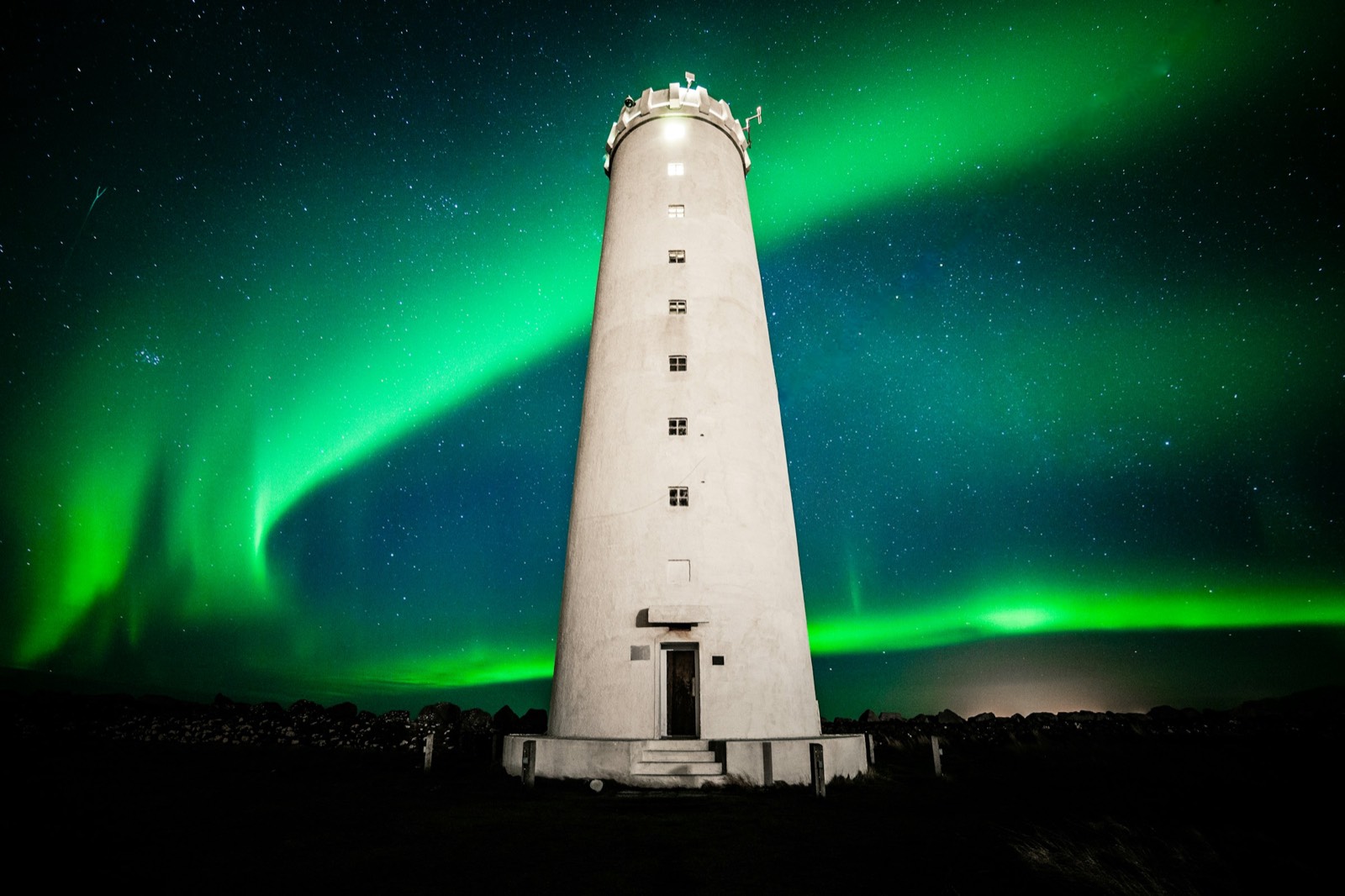 The white Grótta lighthouse on the Seltjarnarnes shore with a green aurora arching behind it