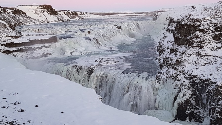 Gullfoss waterfall half-frozen in winter, its canyon walls thick with snow and ice