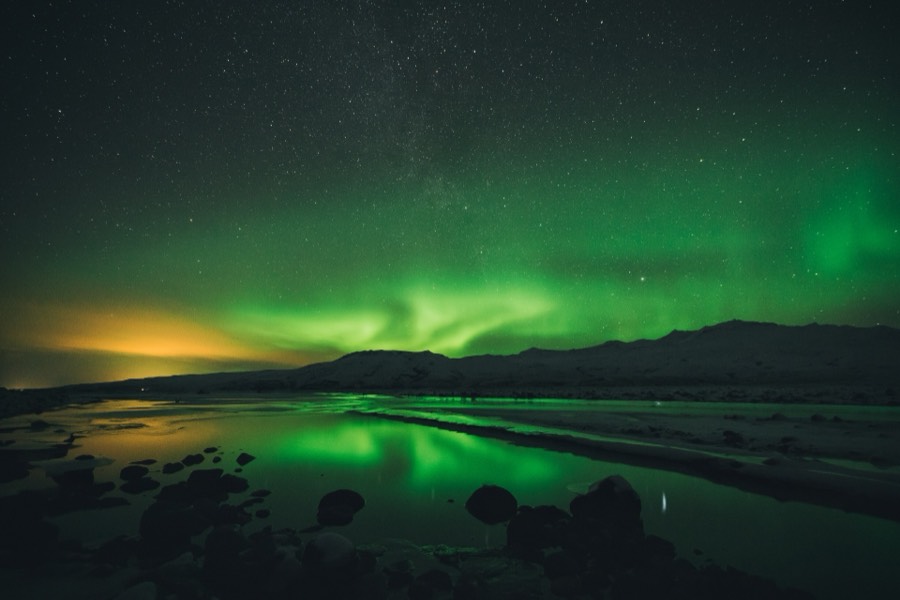 Green aurora reflected in still water beneath a dark mountain ridge in Iceland