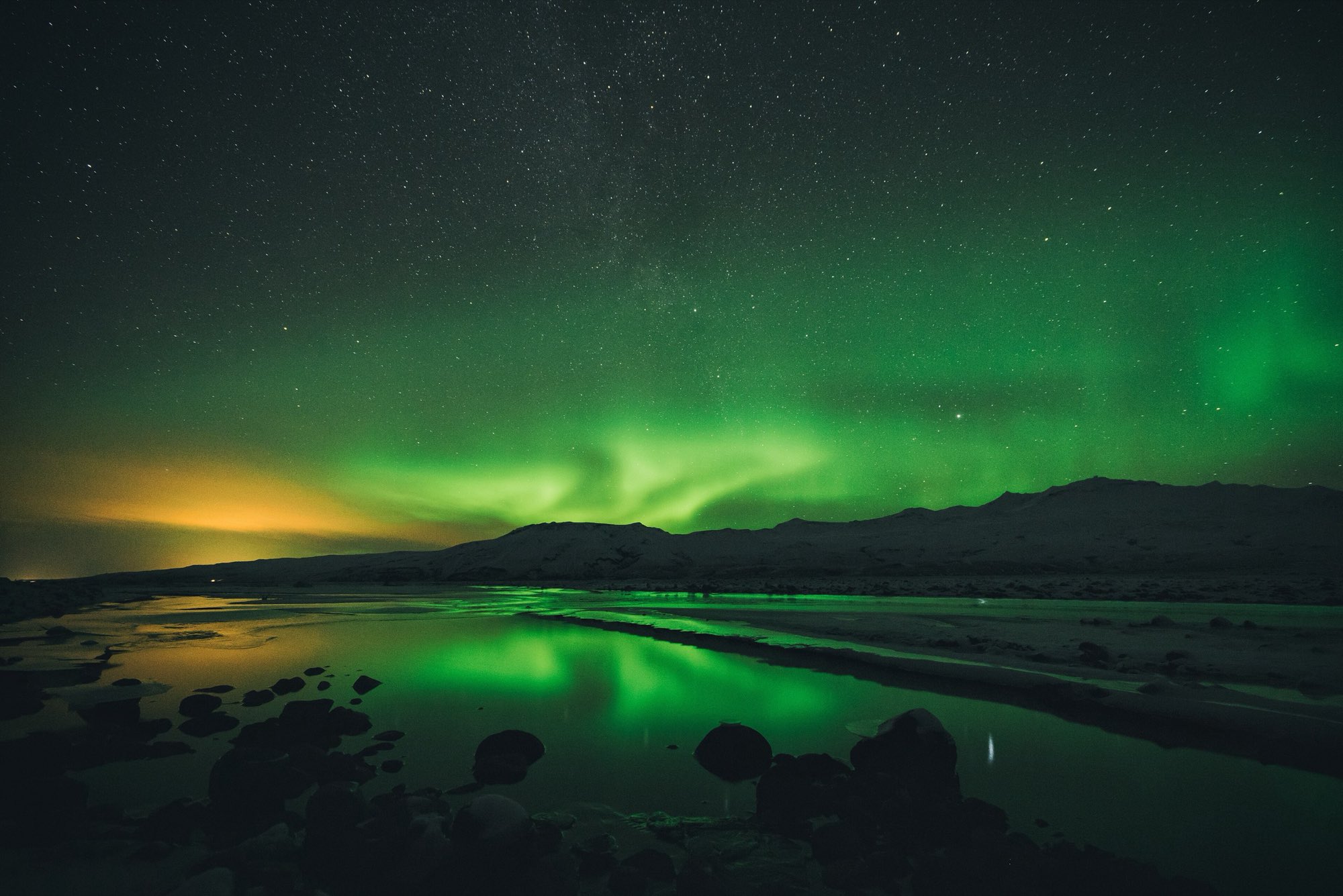 Green aurora reflected in still water beneath a dark mountain ridge in Iceland