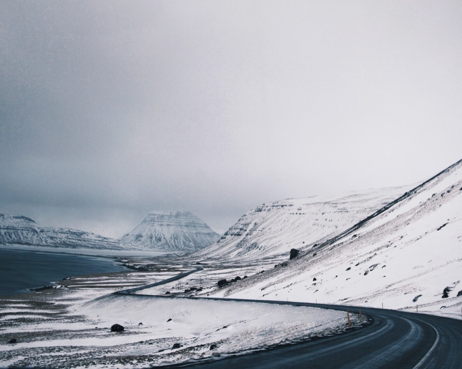A road winding along a snow-covered fjord shore beneath white mountains in Iceland