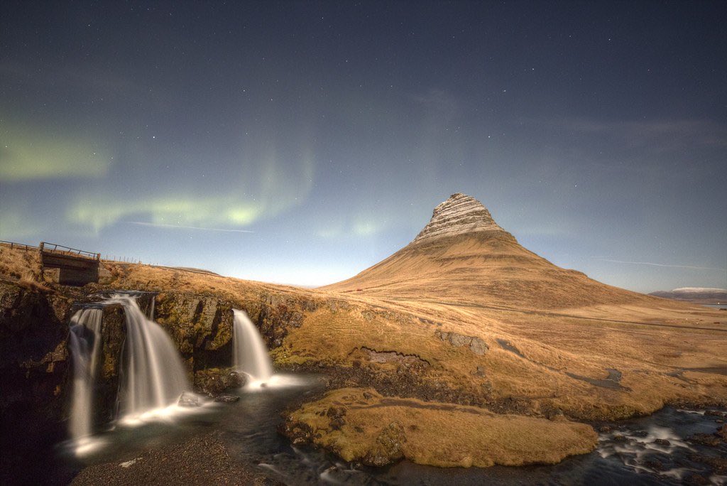 Kirkjufell mountain and the Kirkjufellsfoss falls under a faint green aurora