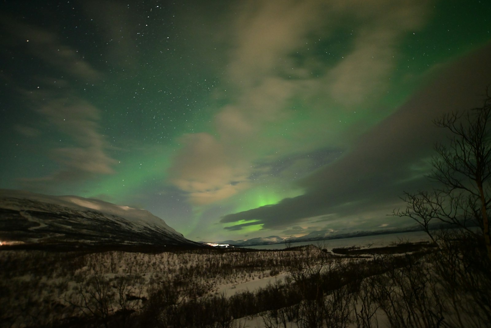 Green aurora showing through gaps in broken cloud over the snowy valley and lake at Abisko