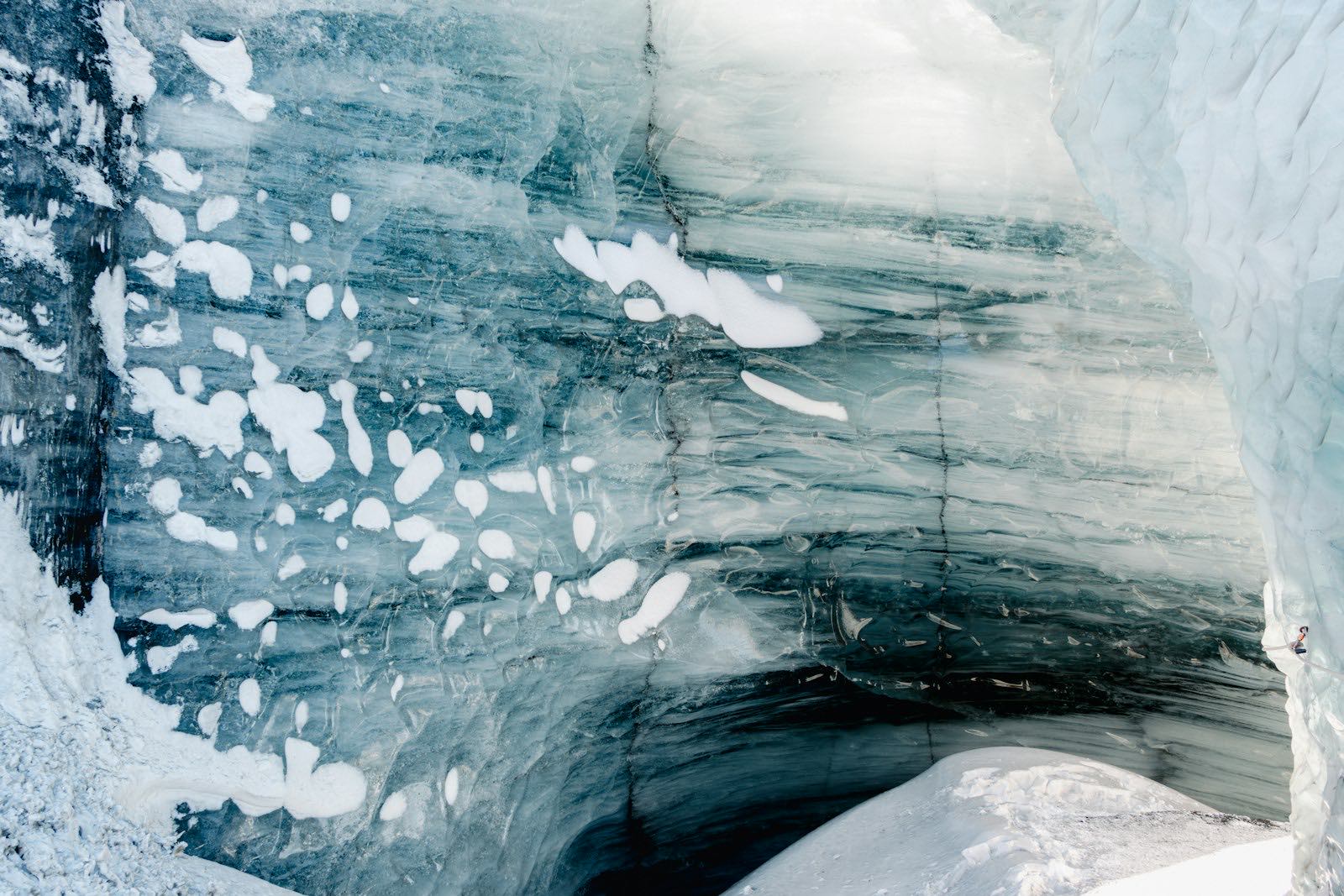 A wall of blue-grey glacier ice banded with dark layers and patched with snow at the mouth of the Katla ice cave