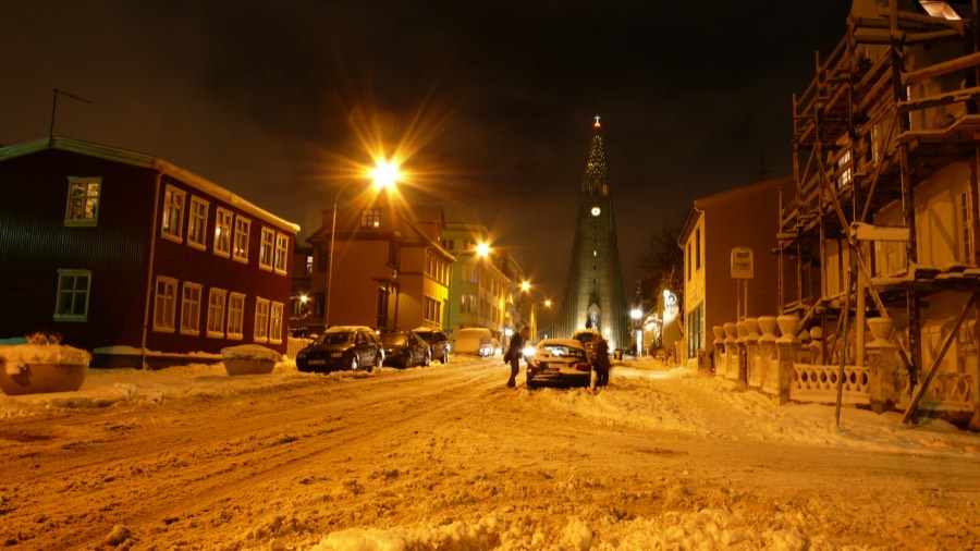 A snowy Reykjavík street at night under orange streetlights, with Hallgrímskirkja lit at the end